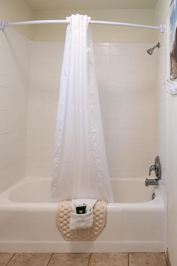 Tiled bathtub with white shower curtain, curved rod, and towel on mat
