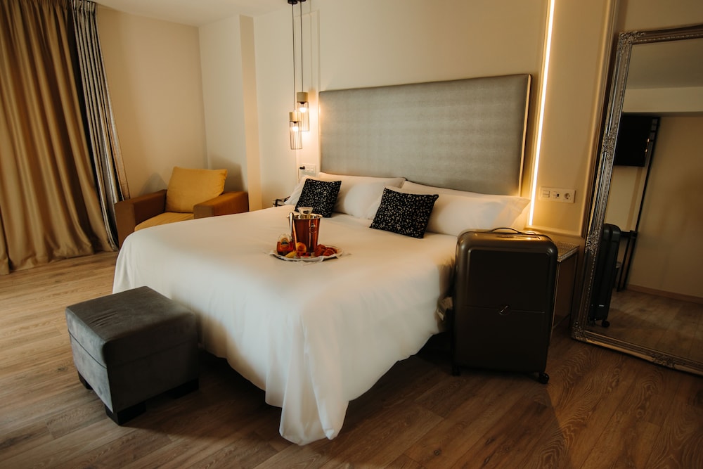 Hotel bedroom with a large bed, white linens, and a gray upholstered headboard.