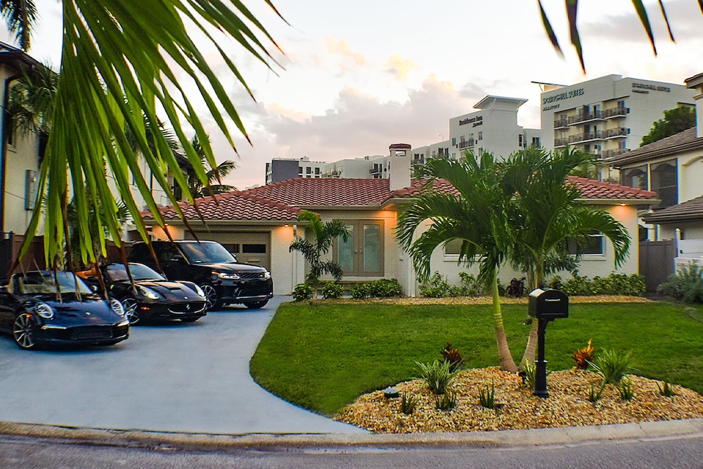 Residential exterior with driveway, cars, lawn, and palm trees